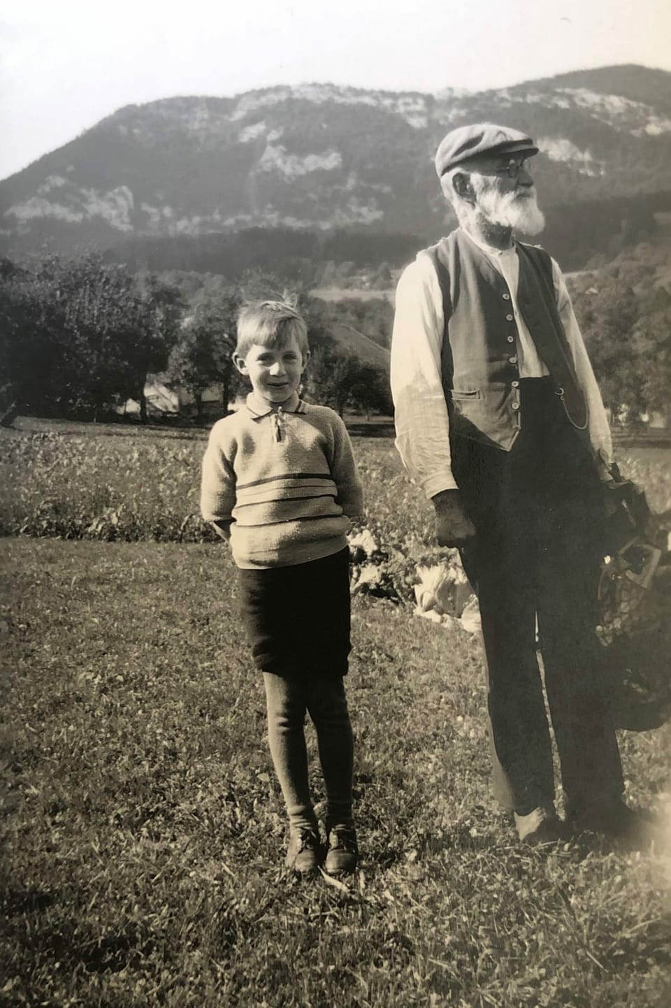 Ein kleiner Junge steht mit seinem Grossvater auf einer Wiese.