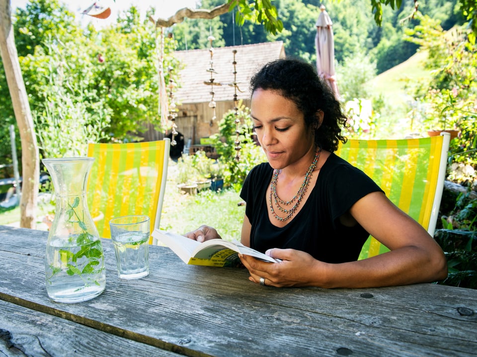 Eine Frau sitzt an einem Tisch und liest ein Buch.