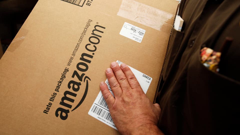Ein Mann hält ein Paket von amazon.com in der Hand.