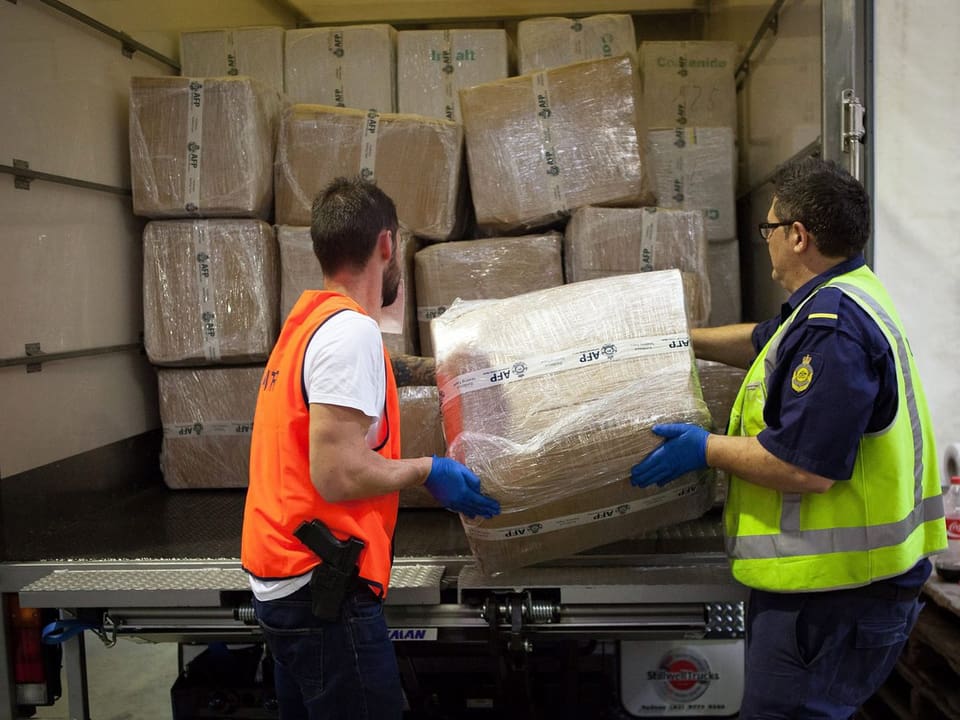 Zwei australische Beamte halten eine Kiste vor einem Container in den Händen 