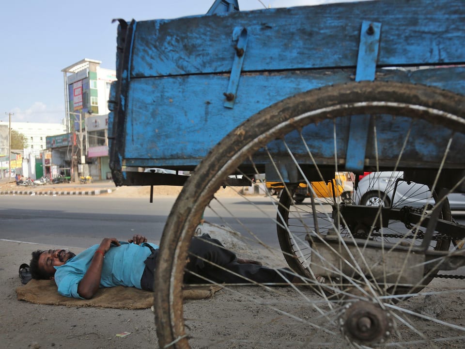 Ein Mann liegt direkt am Strassenrand unter einem Wagen und schläft