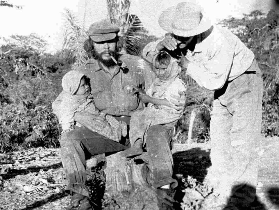 Che Guevara posiert mit zwei Kindern und Zigarre im Mund.