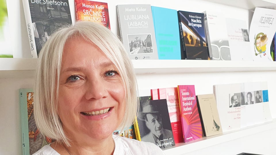 Woman with white, short hair in front of shelves with various books and magazines