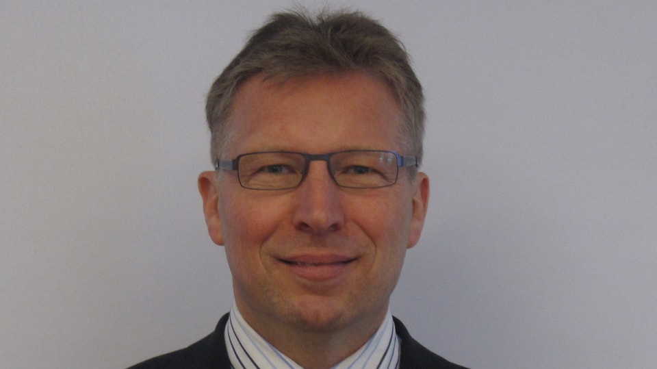 Porträt des Bettinger Gemeindepräsidenten Patrick Götsch. Er lächelt, hat eine Brille und graumelierte Haare.