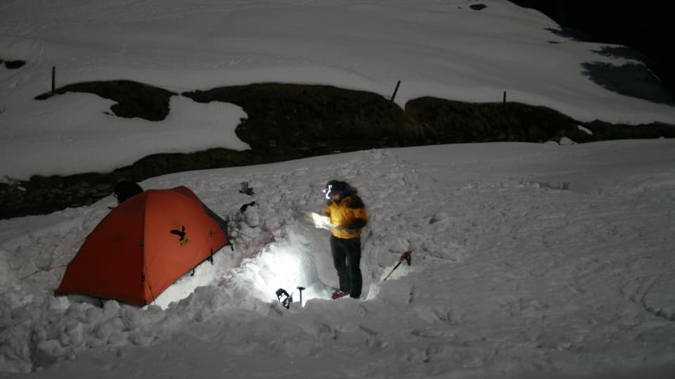 Ein Mann steht neben seinem Zelt im Schnee und schaut auf die Landkarte