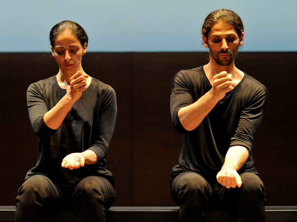 Zwei Tänzer, in schwarz gekleidet, bewegen ihre Hände in der Luft, wie es Töpfer tun. 