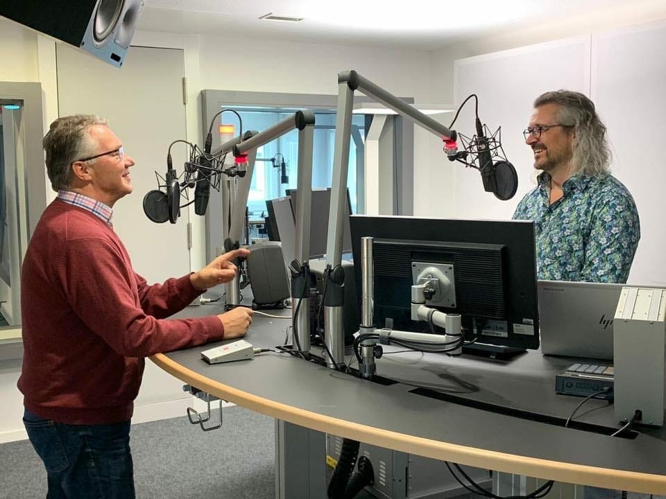 Zwei Männer vor Mikrofonen in einem Aufnahmestudio.