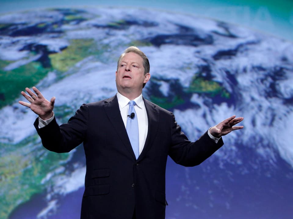 Al Gore steht vor einem Bild der Weltkugel und hält einen Vortrag