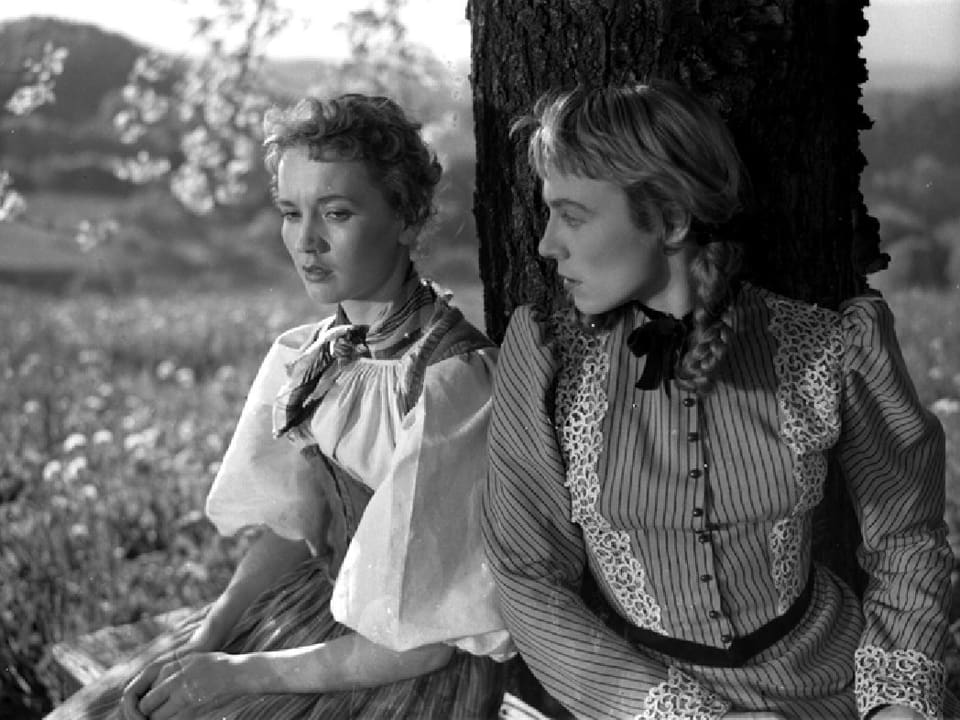Zwei junge Frauen in Bauerntracht sitzen unter einem Baum.