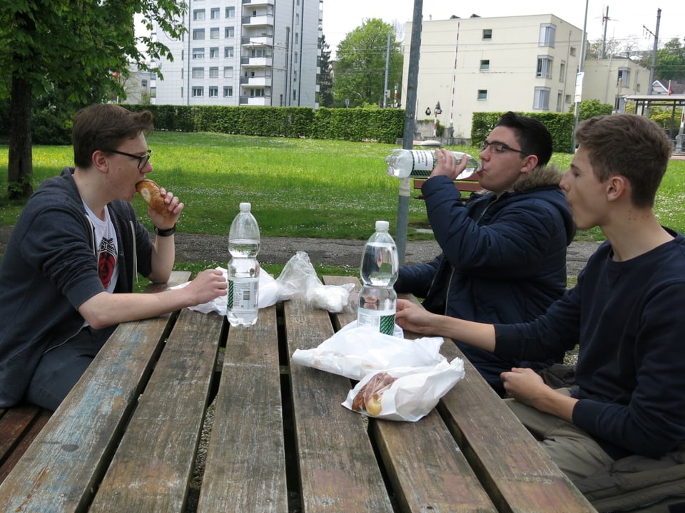 Drei Jugendliche sitzen an einem Tisch im Park und essen