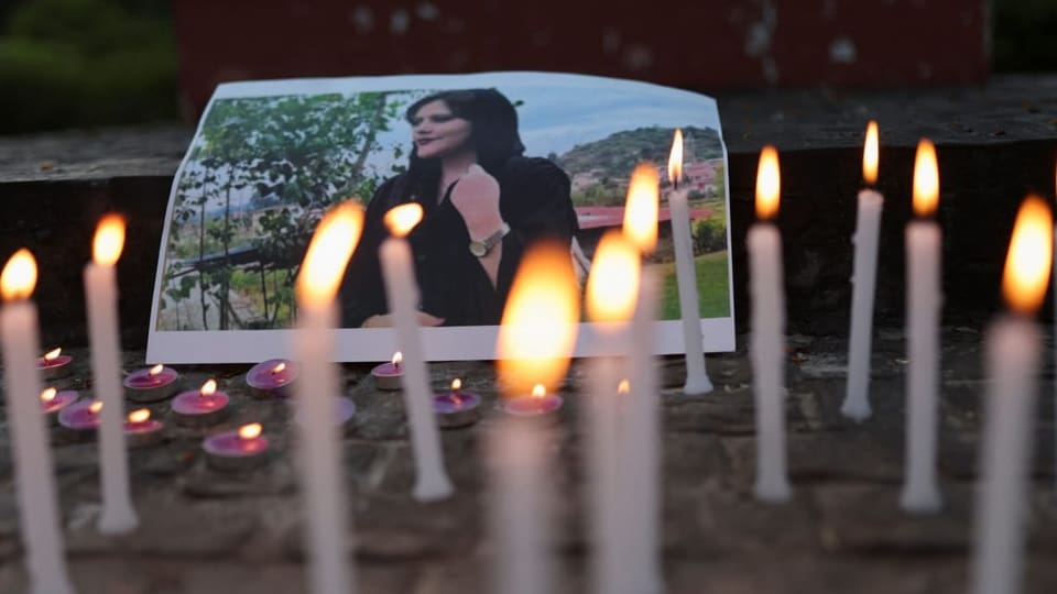 Ein Bild der verstorbenen Mahsa Amini. Es sind brennende Kerzen vor dem Bild.
