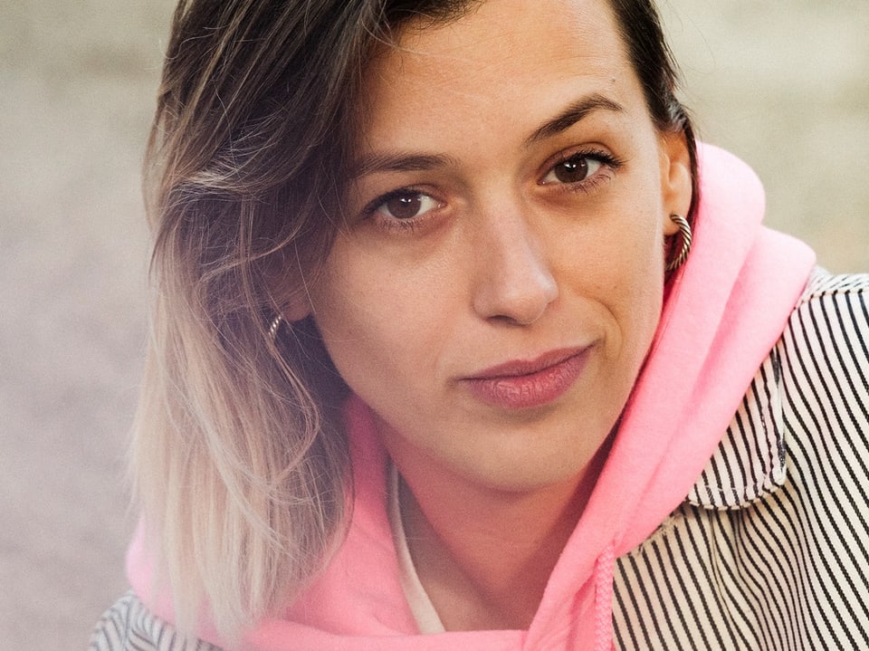 Mulher de moletom rosa com camisa listrada sorri levemente.