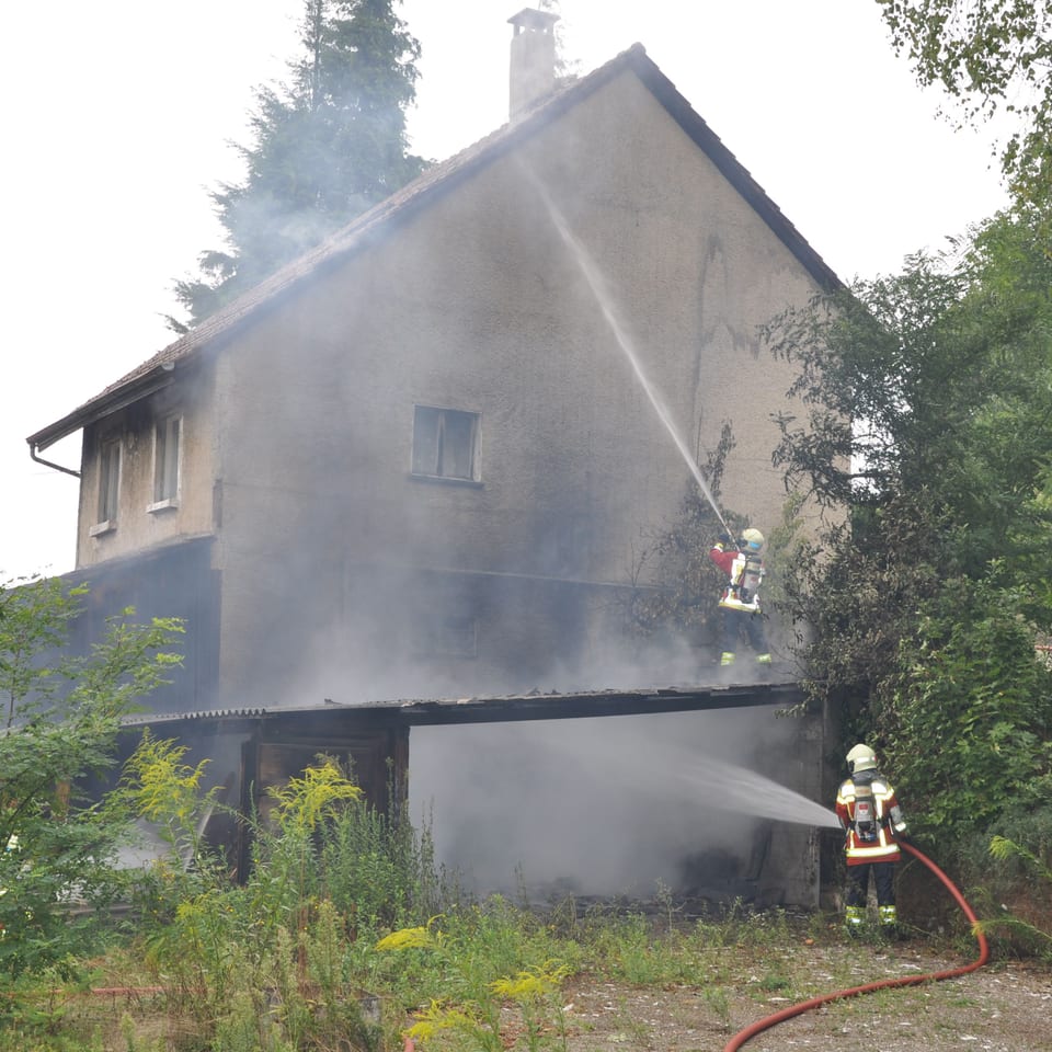 Zwei Feuerwehrleute spritzen Wasser an eine Hausfassade