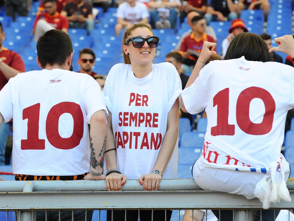 Zwei Fans mit einer 10 auf dem Rücken und eine Zuschauerin mit einem Shirt auf dem «Per sempre Capitano» steht.