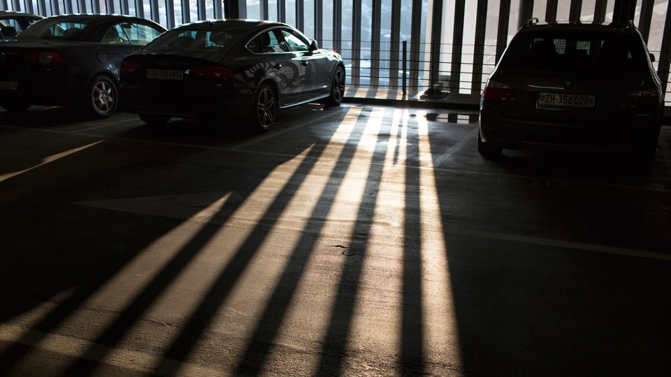 Parklücke in einem Parkhaus, durch dessen halbtransparente Wand Sonnenstrahlen in einem Gittermuster auf den Boden fallen.
