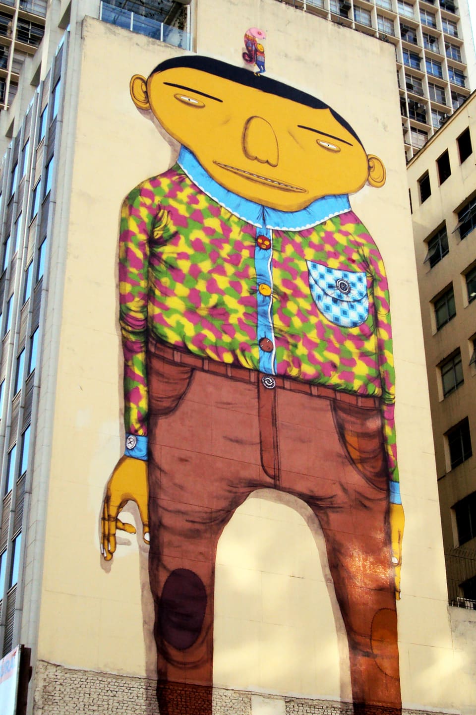 Wandbild: Ein Mann mit grossem, breitem Kopf, langezogenen Augenbrauen, Hemd und Hose.