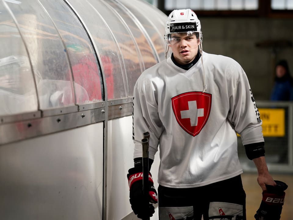 Eishockeyspieler mit Helm und Schweizer Trikot in einer Eishalle.