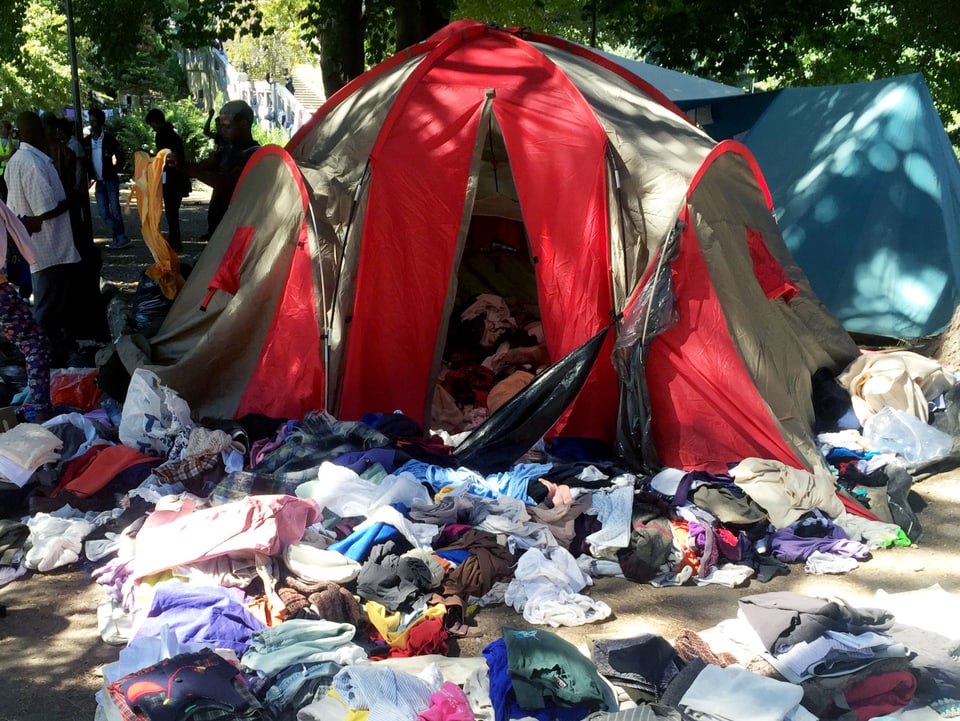 Viele Kleider liegen vor einem Zelt.