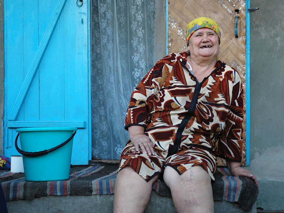 Eine alte Frau sitzt vor ihrem Hauseingang.