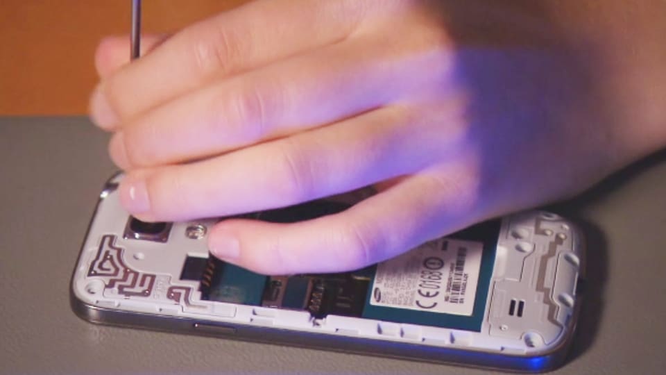 Eine Frau schraubt ein Smartphone auf.