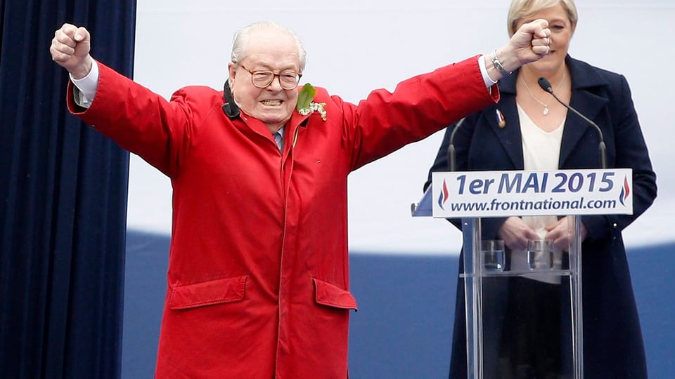 Jean-Marie Le Pen in rotem Mantel mit ausgebreiteten Armen.