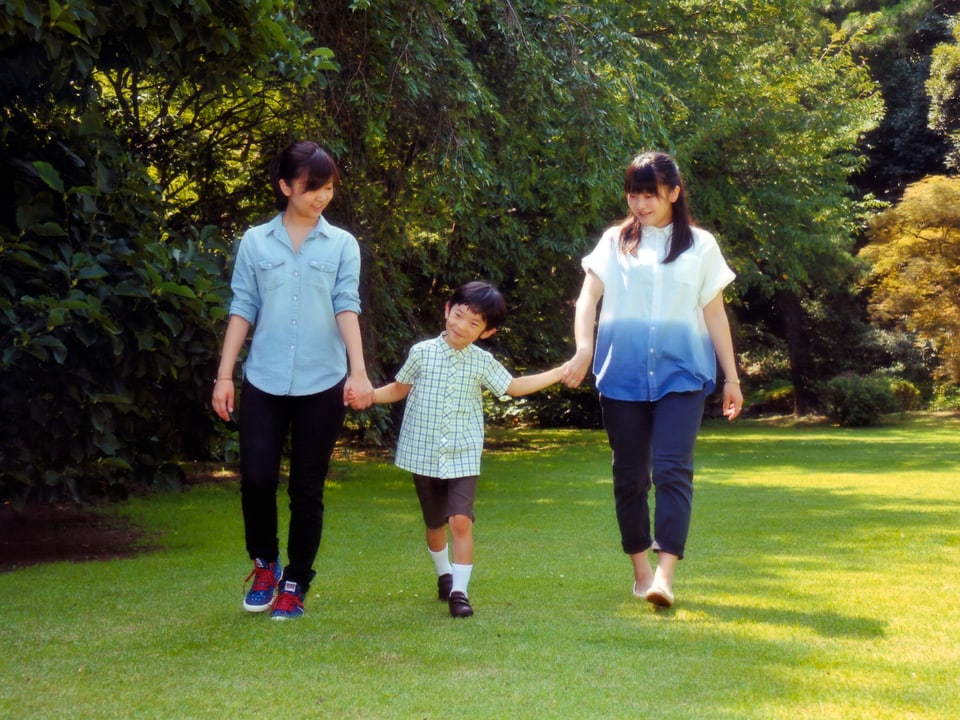 Hisahito (mitte) spaziert an den Händern von seinen beiden Schwestern.