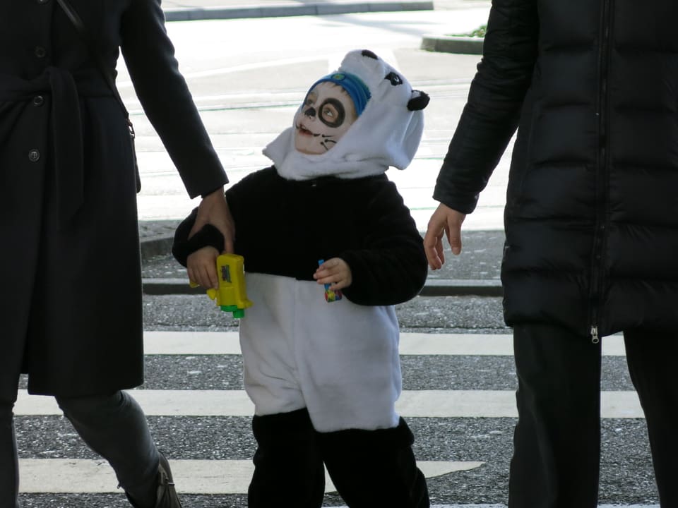 Kind in Pandakostüm zwischen den beiden Eltern.