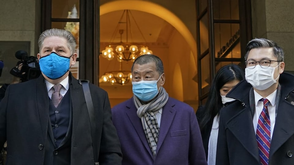 Drei Männer mit Masken kommen aus einem Gebäude.