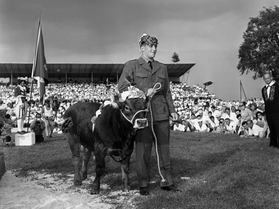 Schwingerkönig Rudolf Hunsperger 1966 bei der Siegerehrung in Frauenfeld. Er tärgt eine Uniform und hält ein Muni am Strick.