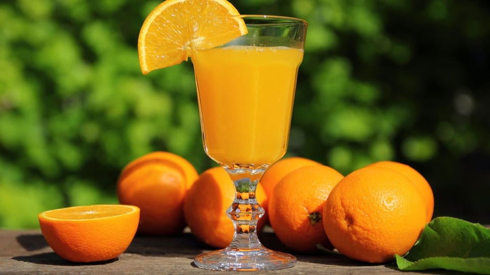 Orangen liegen auf einem Holztisch, davor steht ein Glas Orangensaft