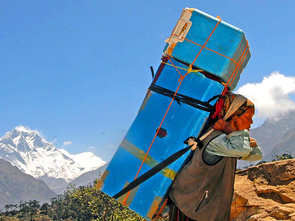 Eine Sherpa trägt ein riesiges blaues Paket auf den Mount Everest.