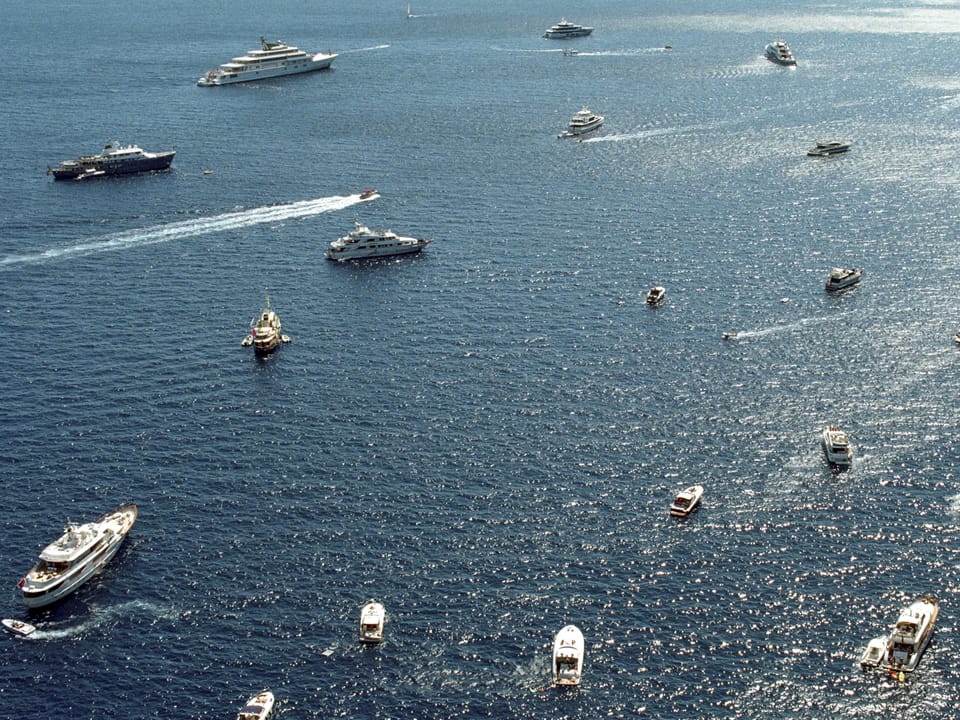 Ein Dutzend Schiffe und Jachten schwimmen aus Vogelperspektive auf dem Meer.