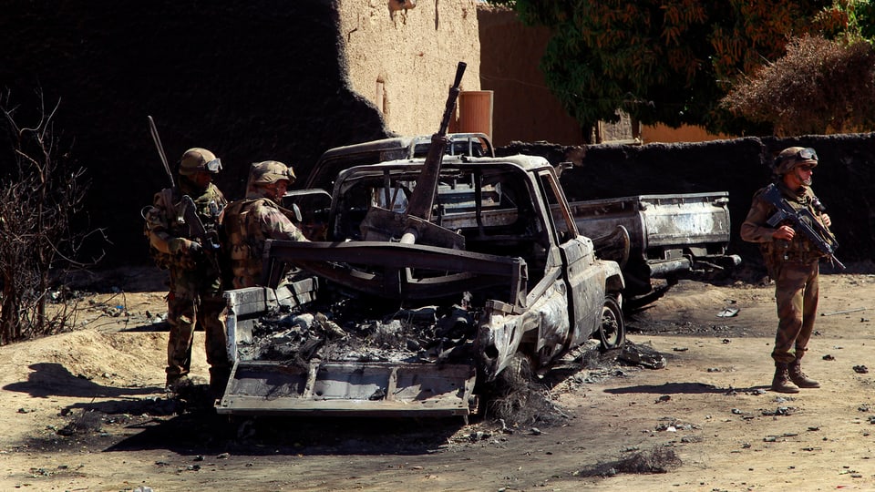 Soldaten vor einem ausgebrannten Pick-Up.