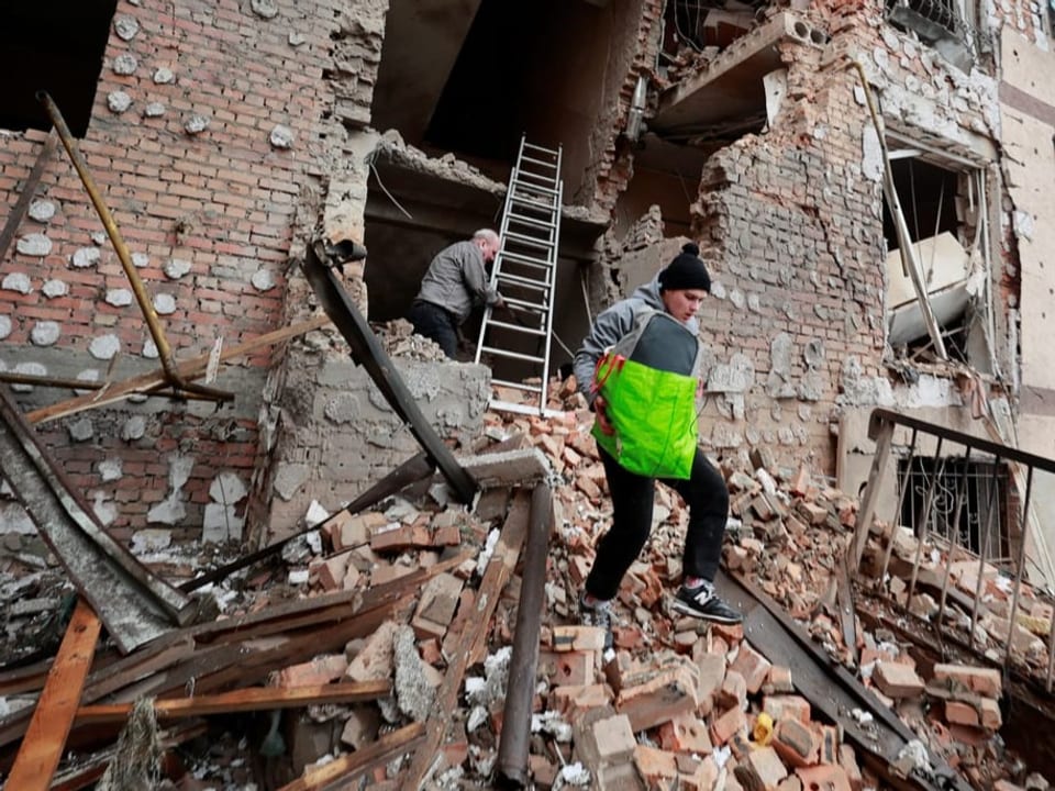 Menschen tragen Habseligkeiten av einem Wohnhaus, das besschuss in Irpin zerstört wurde.
