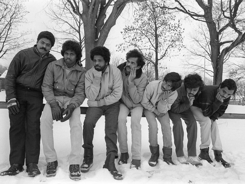 Eine Gruppe tamilischer Asylbewerber sitzt im Schnee auf einer Bank.
