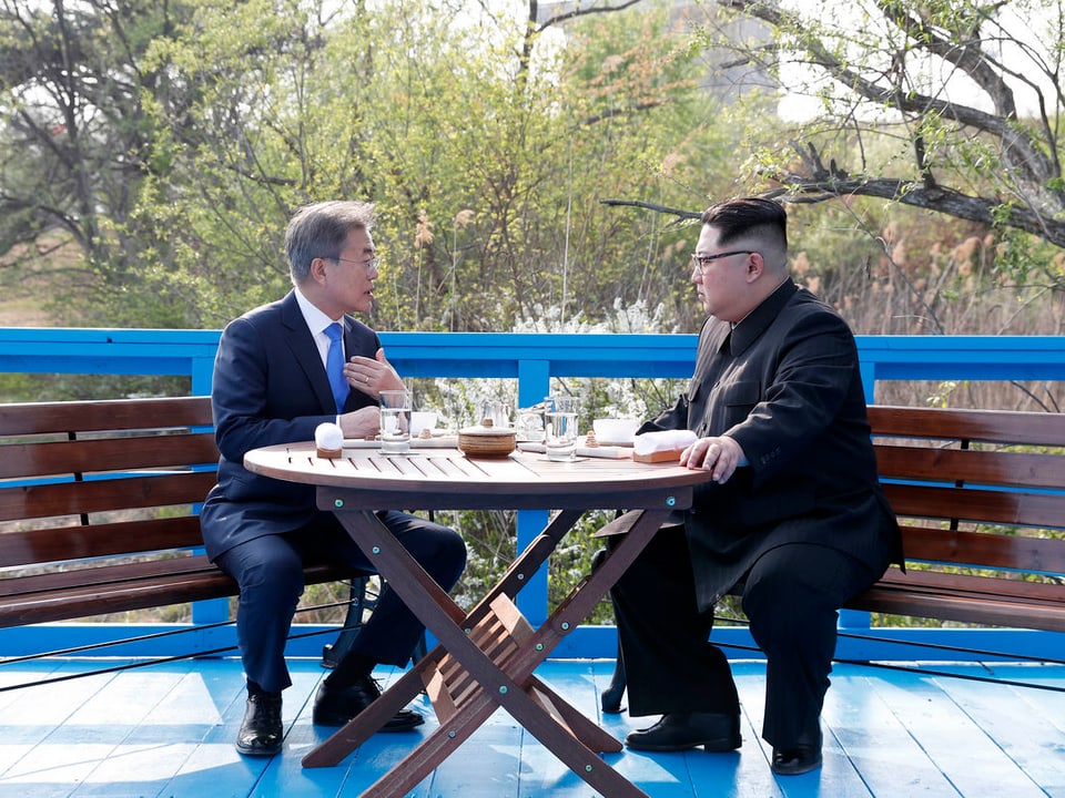Beide Männer sitzen an einem runden Holztisch.