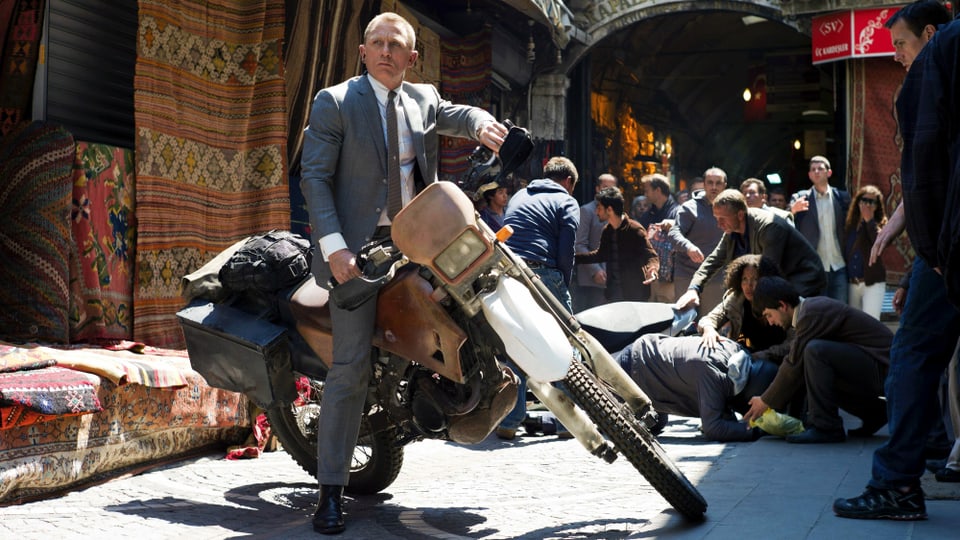 Ein Mann sitzt auf einem Motorrad, im Hintergrund ein Markt.