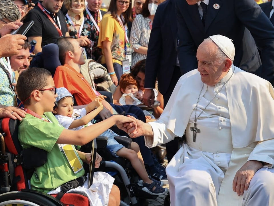 Der Papst, selbst im Rollstuhl, gibt einem Jungen in einem Rollstuhl die Hand. 