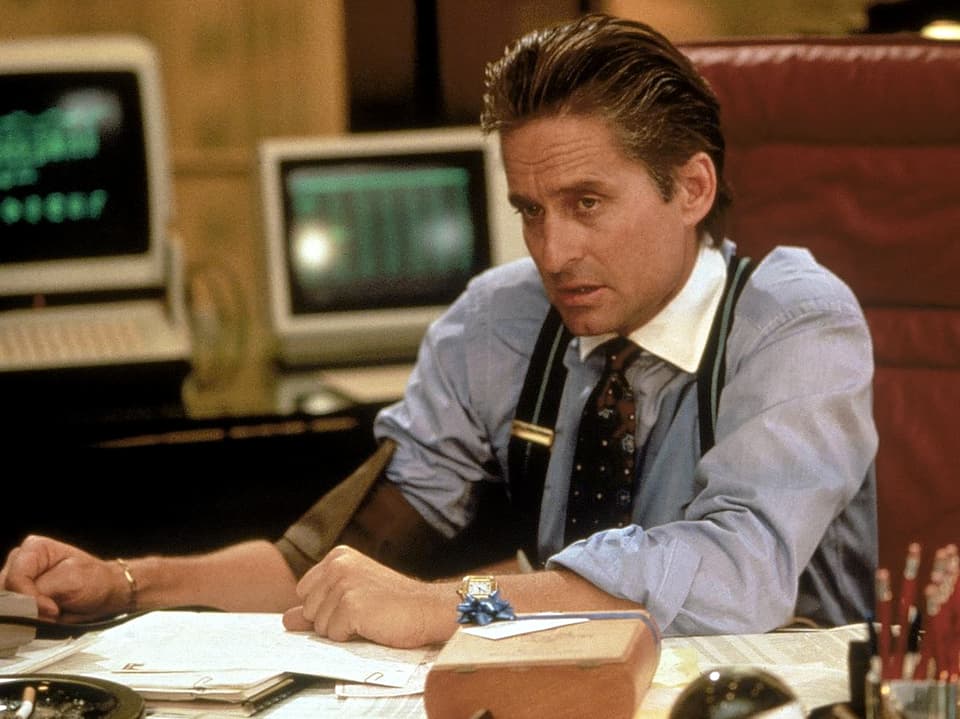 Ein Banker mit Hemd und Hosenträger sitzt an seinem Schreibtisch und schaut kritisch einem Kunden ins Auge.