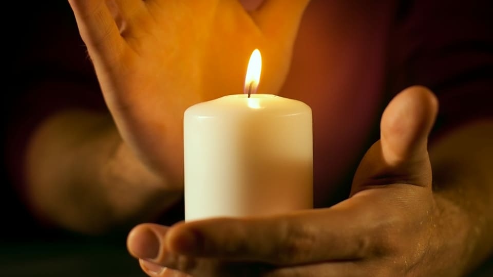 Eine Hand umfasst eine brennende Kerze.
