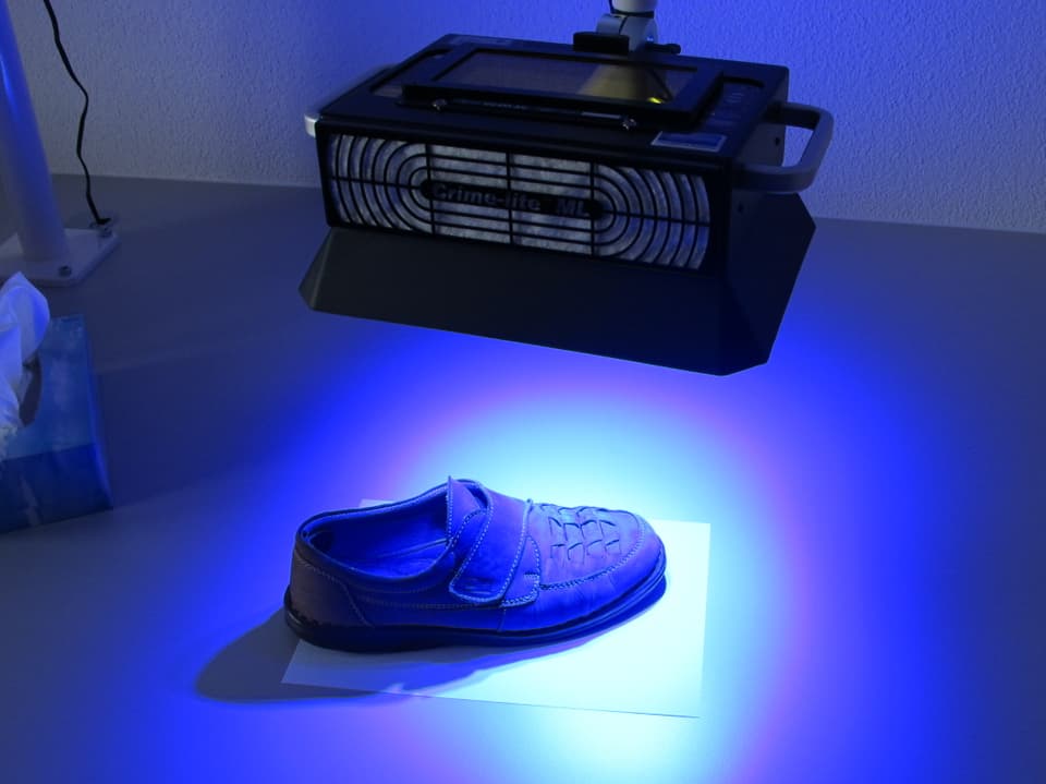 Schuh auf einem Tisch, darüber eine Lampe, die blaues Licht produziert
