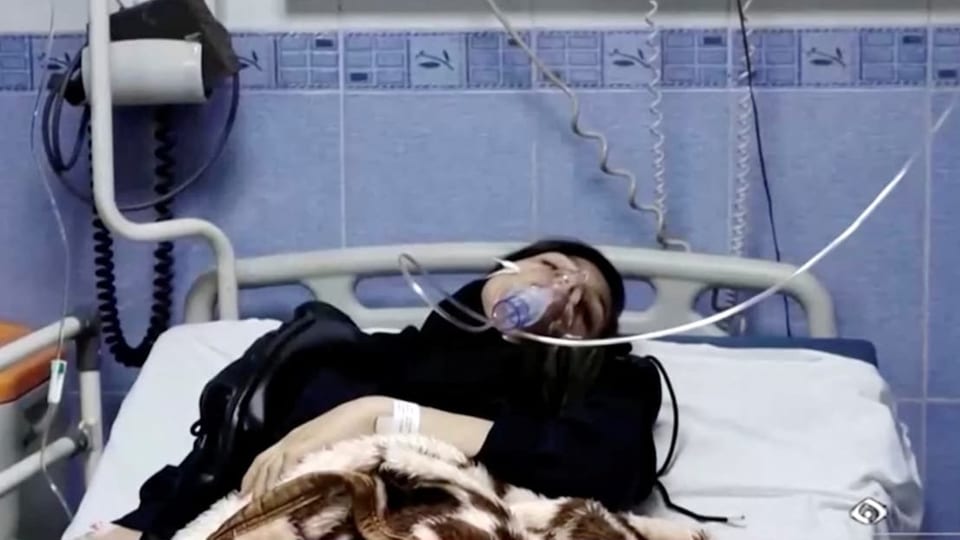 Eine Frau liegt auf einem Krankenbett mit einer Beatmungsmaske.