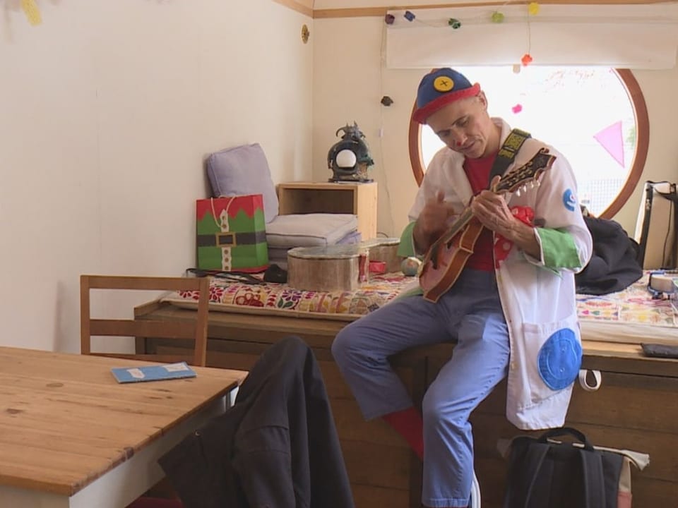 Als Clown verkleideter Mann spielt auf einer kleinen Gitarre.