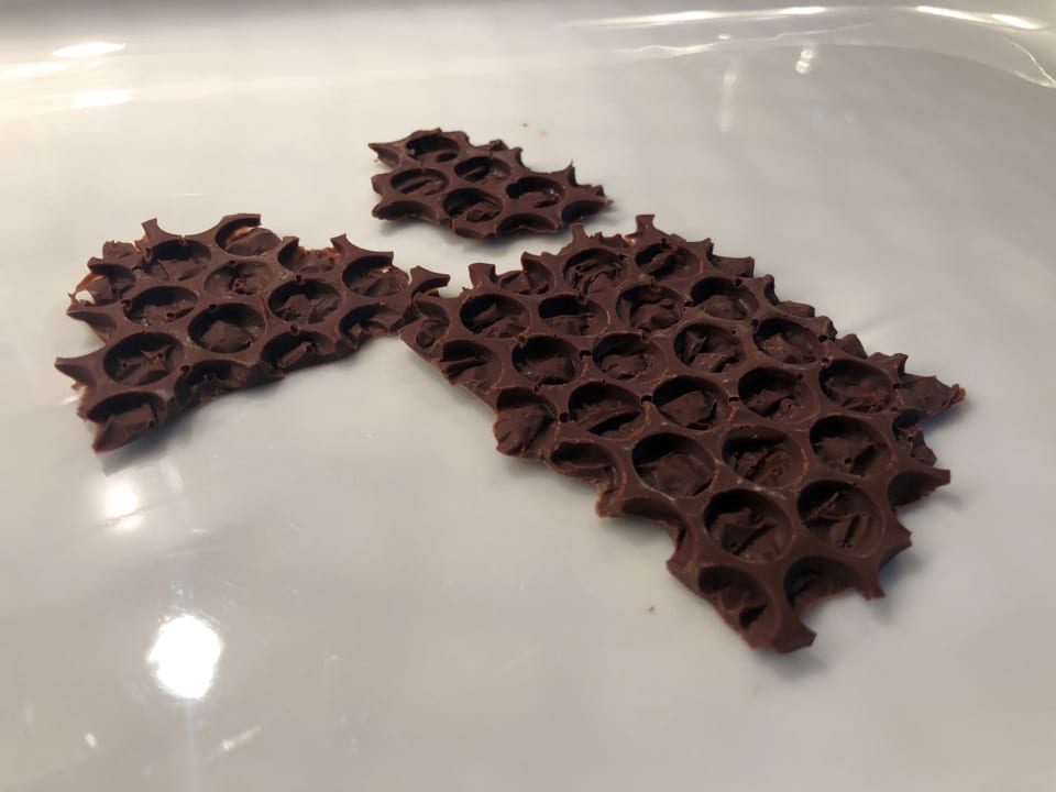 Auf einem Teller liegen Schokoladen-Plättchen, die einer Bienenwabe gleichen. 