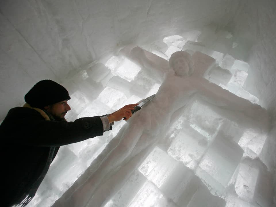 Ein Eis-Skulpteur bearbeitet eine Christus-Statue mit einem Messer.