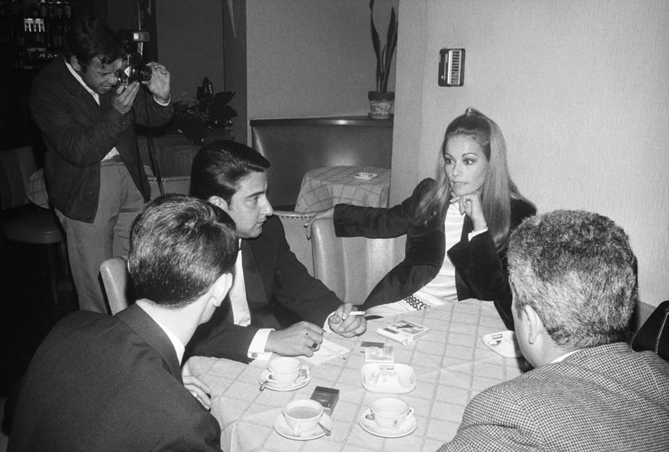 Black and white photo: elegant woman talking to reporters at a table