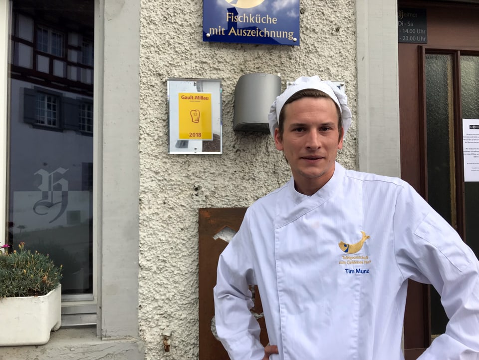 Junger Mann steht mit Kochmütze vor Gault Millau-Tableau draussen an der Tür