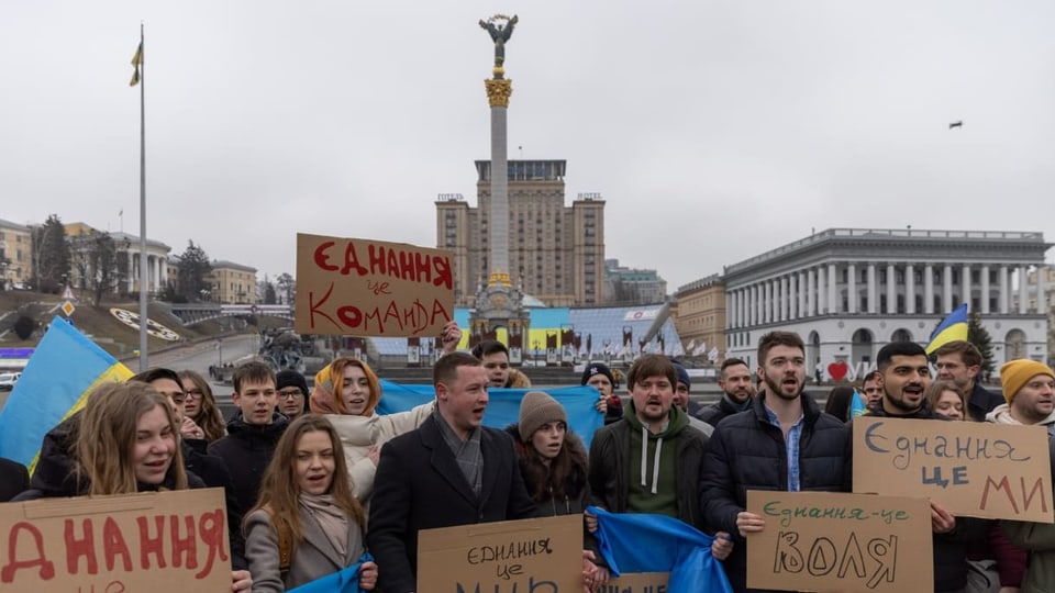 Protestierende halten Schilder und die ukrainische Flagge hoch