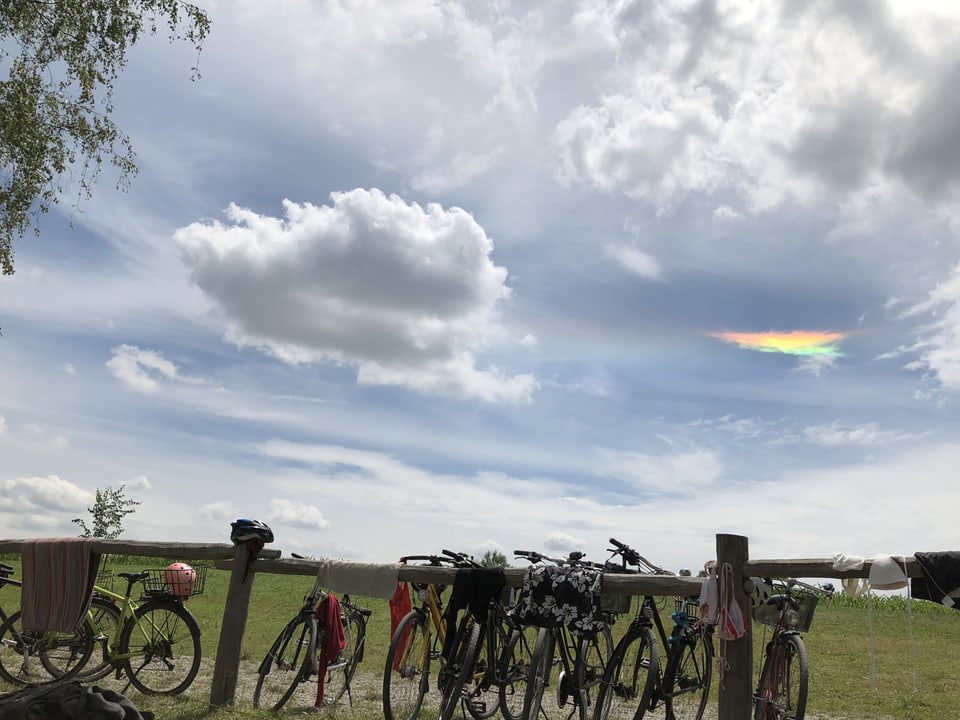 Geländer mit Fahrrädern, darüber Himmel mit verschiedenen, auch farbigen Wolken.
