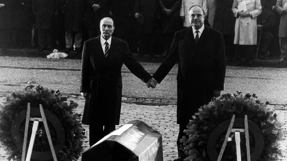 Mitterrand und Kohl halten sich vor Kränzen an der Hand